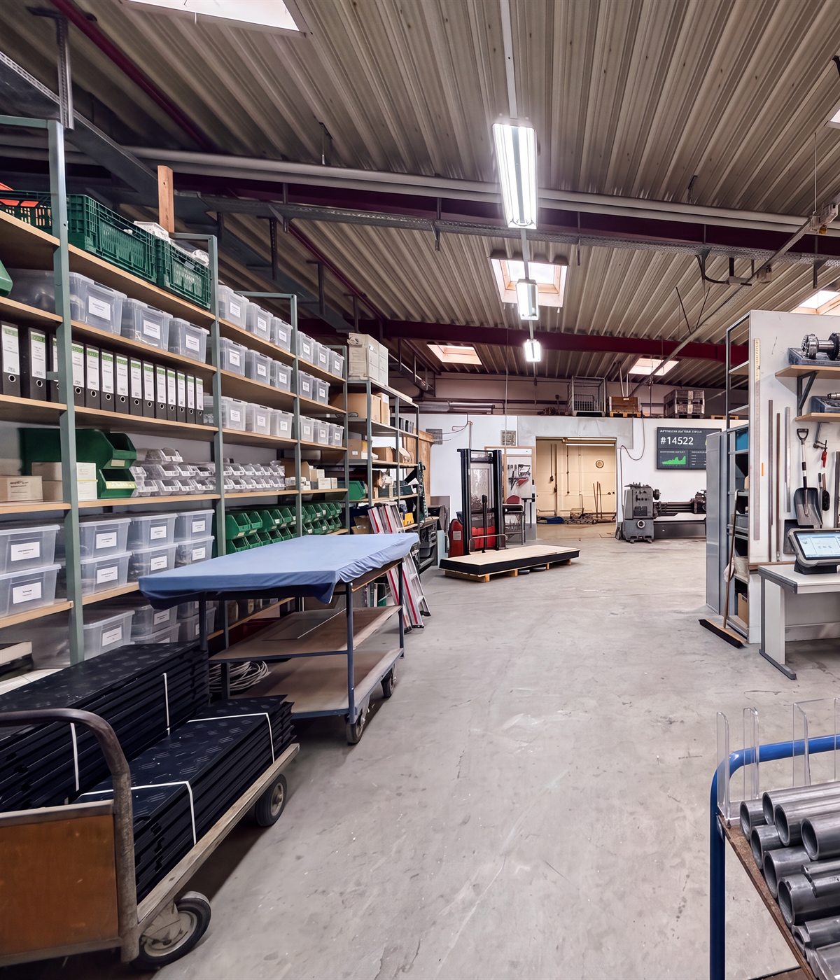 Materiallager mit sortierten Regalen, Plattenstapeln und einem Wagen mit PVC-Rohren